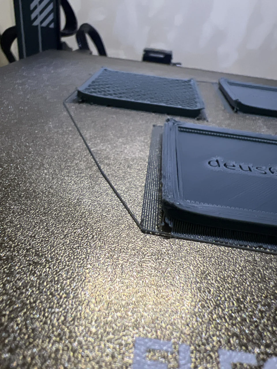 Early grey frame prototypes surrounded by brims on a 3D printer bed